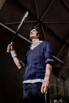 一名留着胡子的白人男子身穿复古网球服，在室内手持球拍