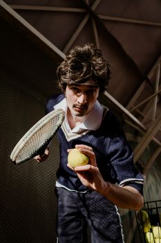 Vintage style tennis player with racket and ball posing indoors with intense focus.