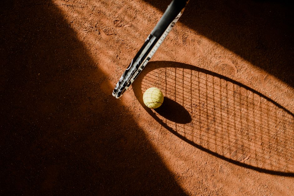 Tennis ball with racket shadow on a sunlit clay court.