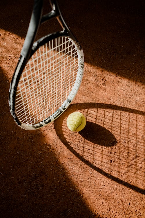 Tennis Ball on Tennis Court beside Black and White Tennis Racket