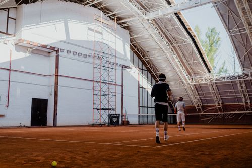 Free Two players engaging in a tennis match on an indoor clay court with natural lighting. Stock Photo
