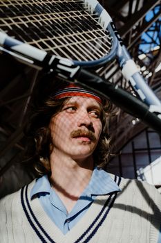 A stylish portrait of a man with vintage tennis gear under dramatic shadows.