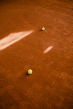 Tennis balls scattered on a clay court with dramatic lighting and shadows.
