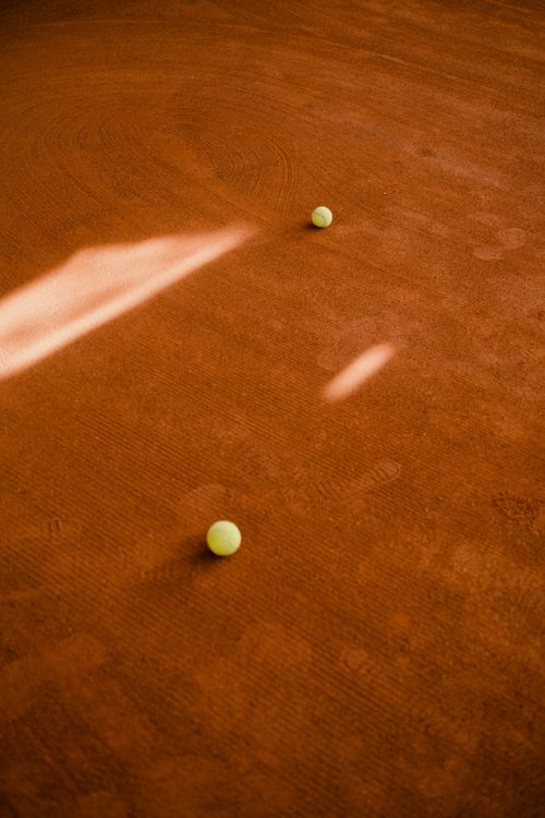 Free Tennis balls scattered on a clay court with dramatic lighting and shadows. Stock Photo