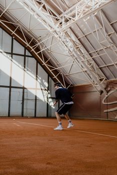 Dynamic shot of a tennis player in action on an indoor clay court with unique architectural ceiling.