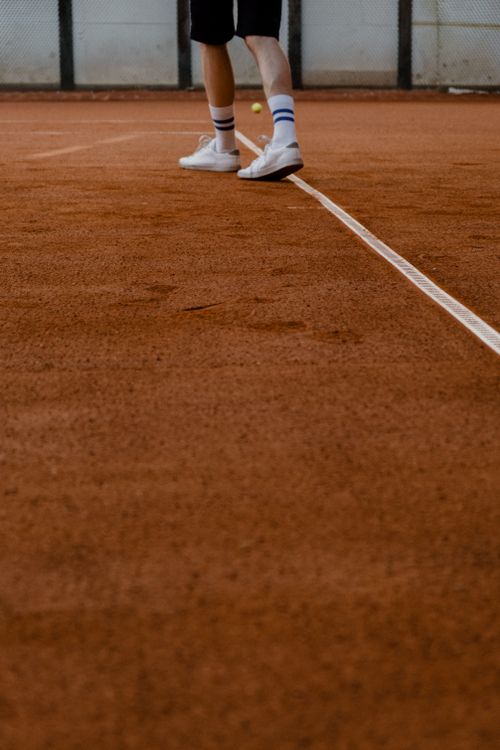Free Close-up of an athlete's legs on a clay tennis court wearing sportswear and white sneakers. Stock Photo