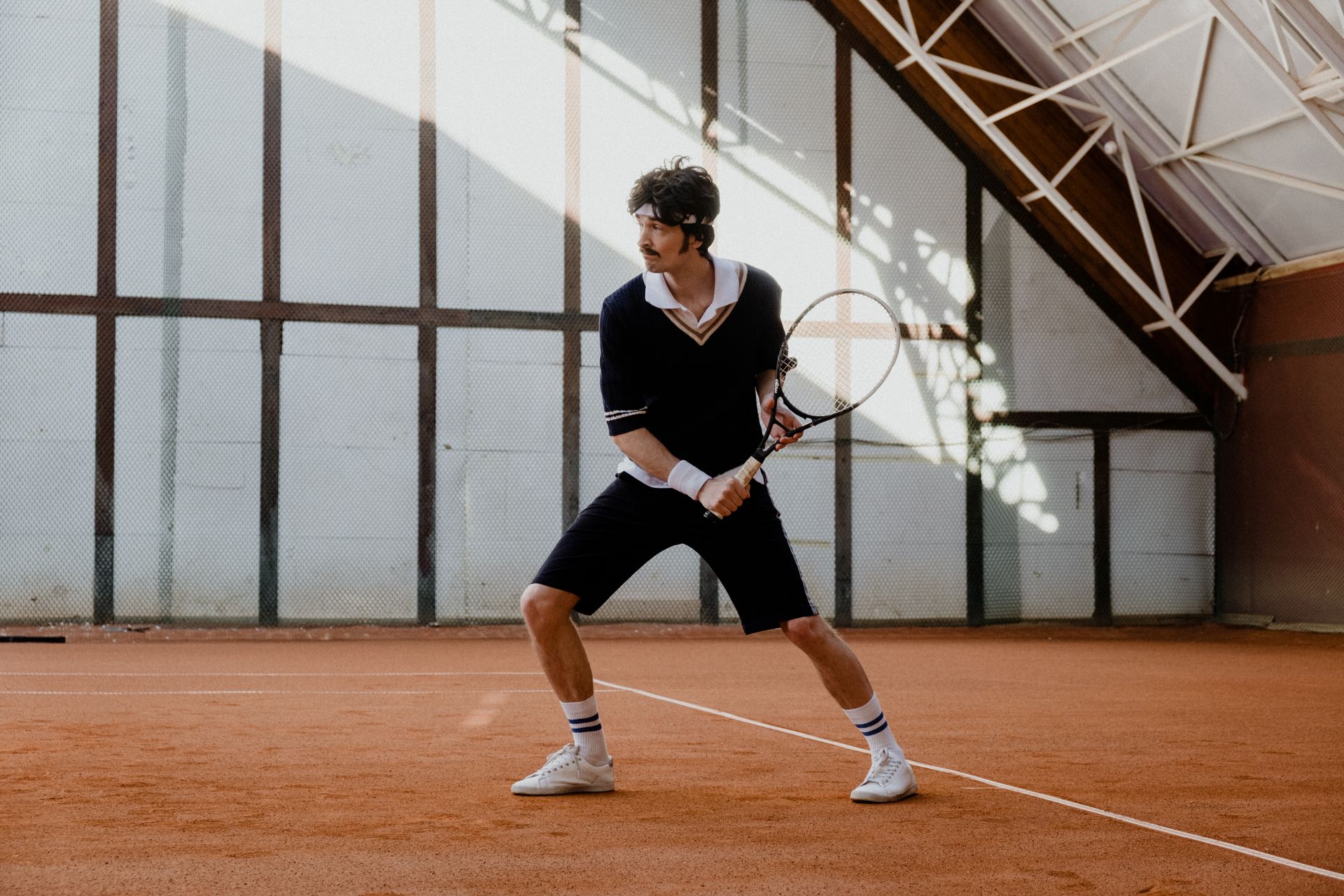 Athletic man poised for action during a tennis match on an indoor clay court.