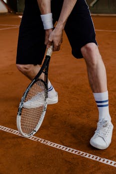 Close-up of a tennis player holding a racket, ready to serve on a clay court.
