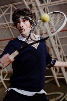 A young adult male tennis player energetically returning a ball on an indoor court.