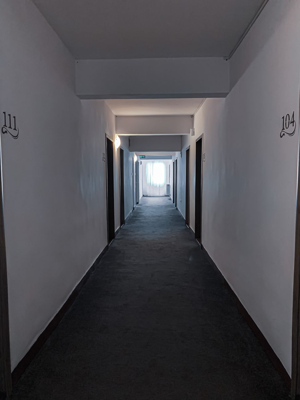 Perspective view of empty hallway with doors and numbers on white walls with window at end of corridor in building. pexels, p