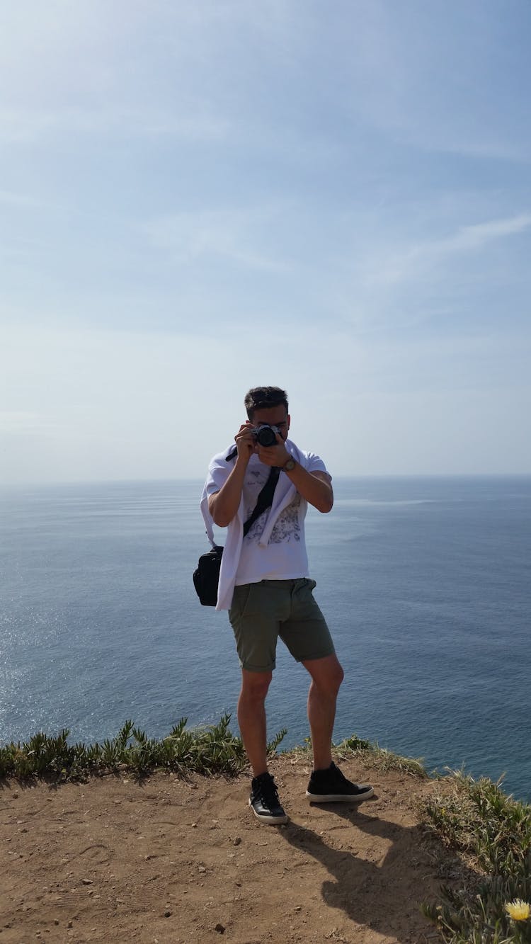 Young Man Standing On Rock Edge Taking Picture