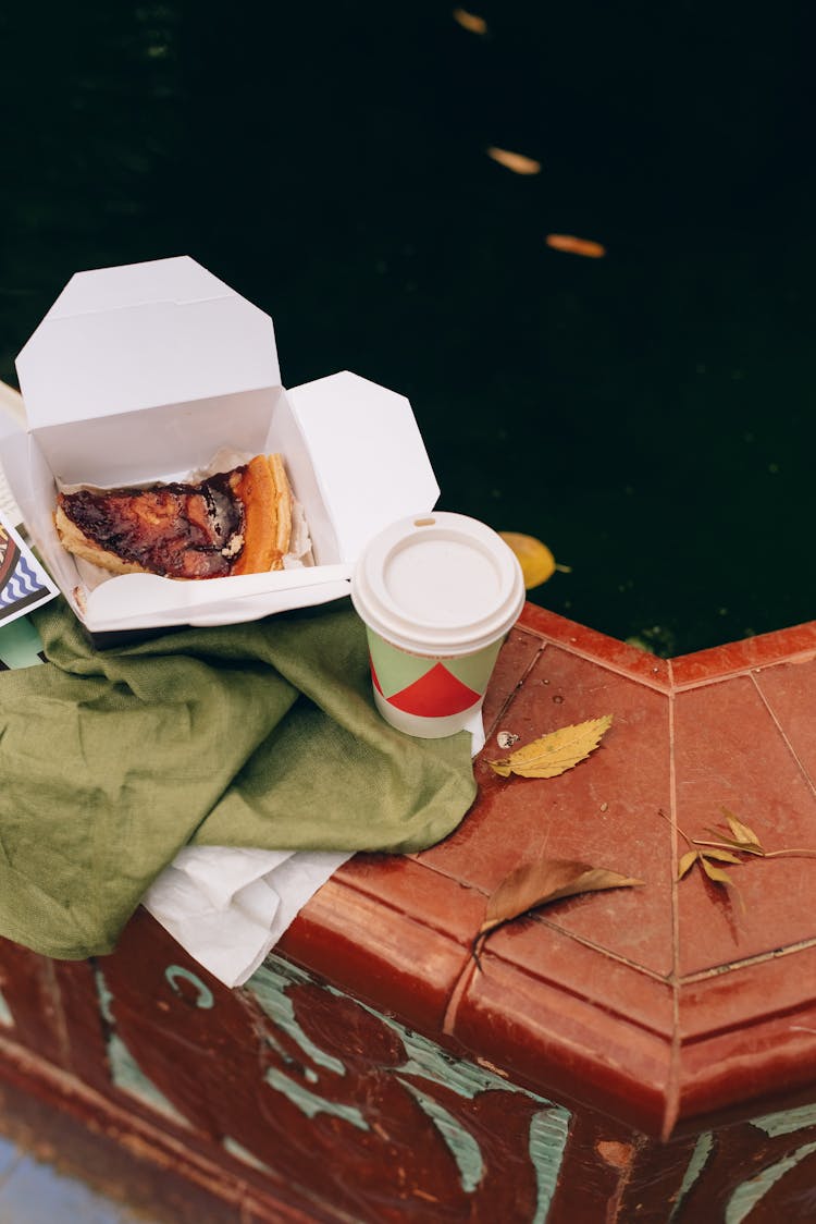 A Cup Near A Takeout Box With A Slice Of Pie