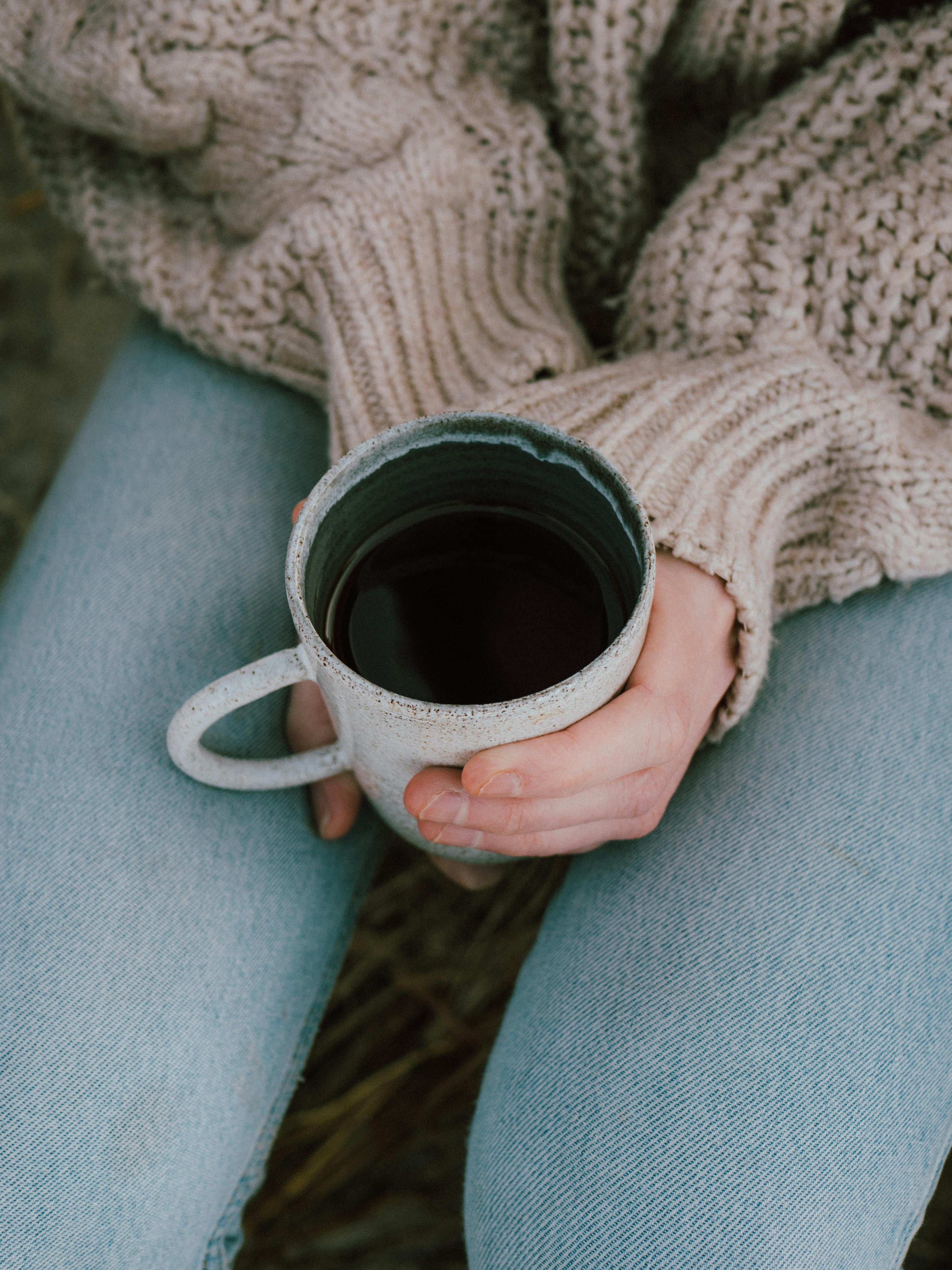 Woman holding coffee in a mug, dressed warmly in fall attire, cozy setting.
