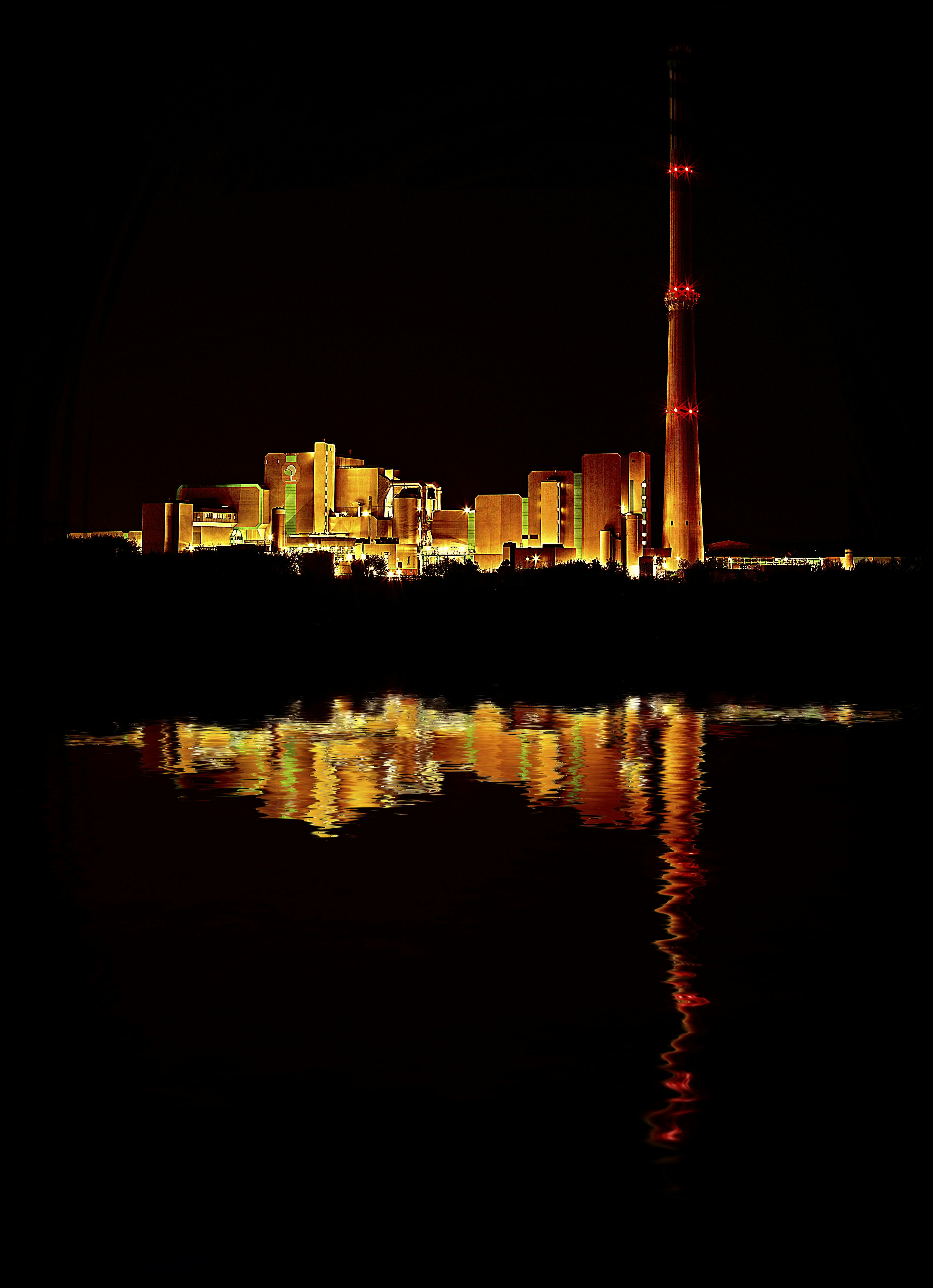 工业综合体的明亮灯光在夜间倒映水中，展现出建筑的辉煌