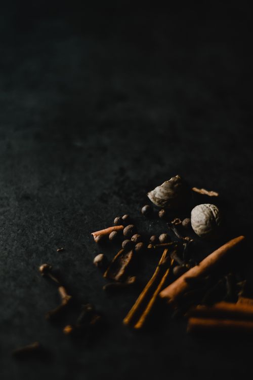 Free A dark, atmospheric flat lay of assorted spices including nutmeg and cinnamon sticks on a textured surface. Stock Photo