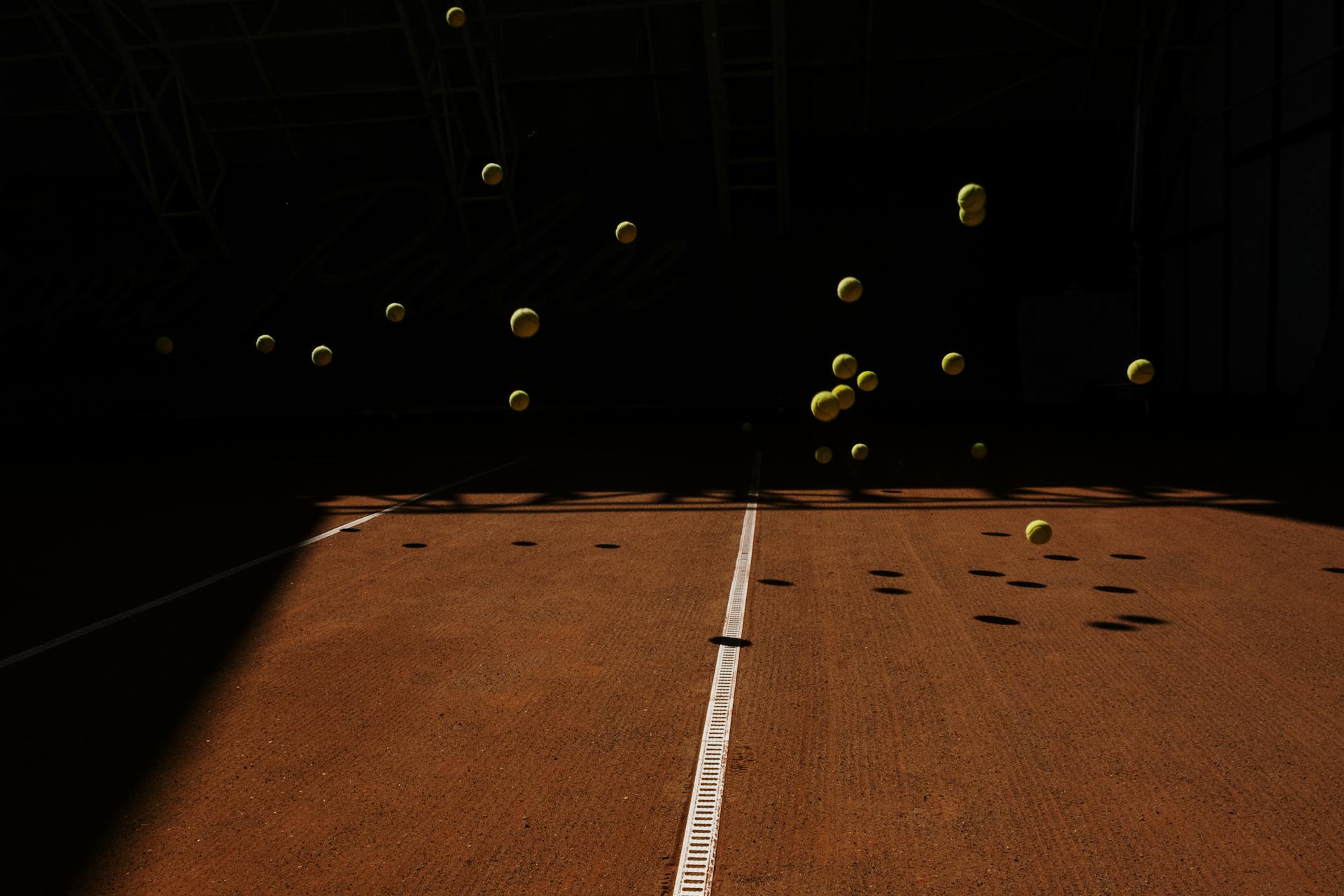 Dynamic shot of tennis balls bouncing on an indoor court, casting shadows.