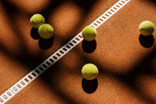 Tennis balls cast shadows on a clay court, showcasing light play and sports ambiance.