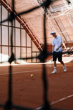 Adult male tennis player on an indoor clay court preparing for a shot.