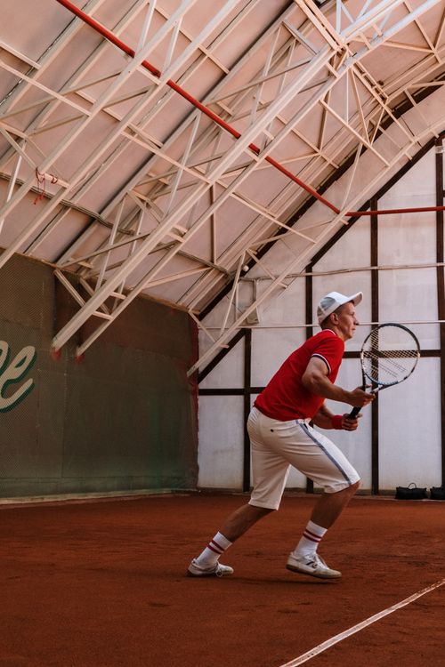 Free Male tennis player in action on an indoor clay court, poised to serve. Stock Photo