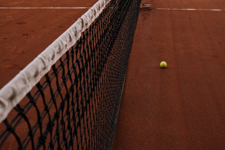 Yellow Tennis Ball Lying On Clay Court By Net