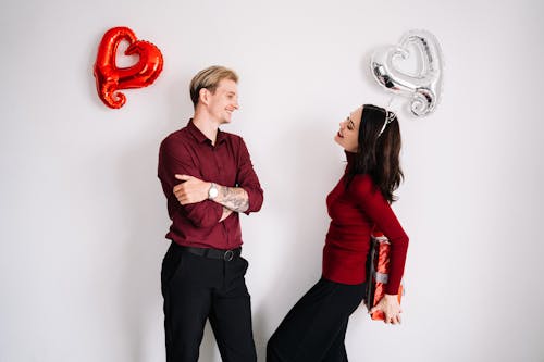 Donna In Camicia A Maniche Lunghe Rossa E Pantaloni Neri In Piedi Accanto Al Muro Bianco