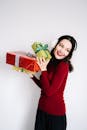 一位喜庆的女人穿着红色毛衣，在白色背景下快乐地拿着包装好的圣诞礼物