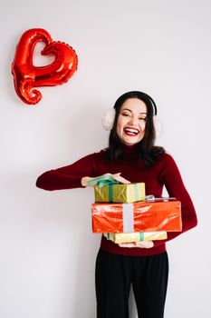 一位戴着耳罩、身穿红色毛衣的快乐女人，微笑着拿着圣诞礼物，旁边有心形气球