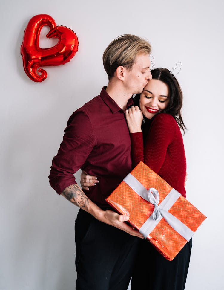 A Man Kissing A Woman While Holding A Gift Box