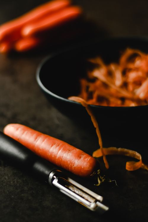 Free Close-up of carrot preparation with peeler and veggie scraps in a kitchen setting. Stock Photo