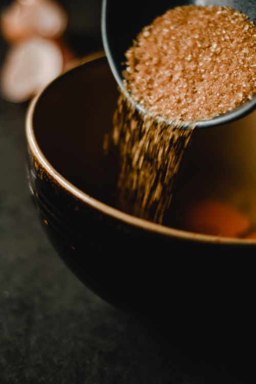 Free Close-up of brown sugar being poured into a dark ceramic bowl, creating a sweet and rustic feel. Stock Photo