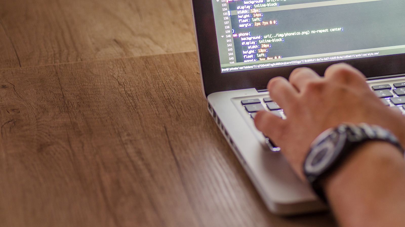 A hand typing on a laptop keyboard with lines of code visible on the screen