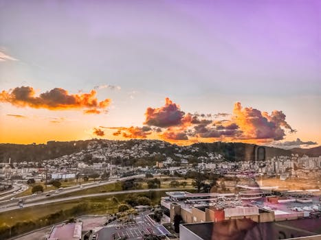 A beautiful cityscape view during sunset, showcasing colorful clouds over urban hills.