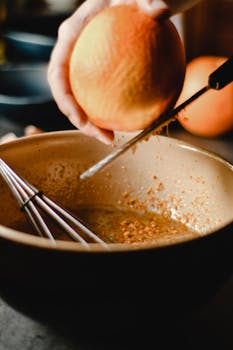 Close-up of zesting an orange into a bowl for cooking, emphasizing fresh citrus aromas.