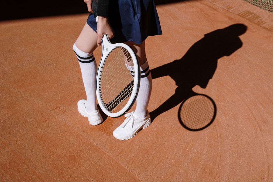Tennis player in a skirt and white sneakers holding a racket in sunlight