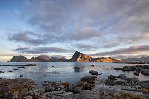 Spectacular scenery of mountains on rocky coast of rippling sea against cloudy sundown sky in Lofoten Archipelago