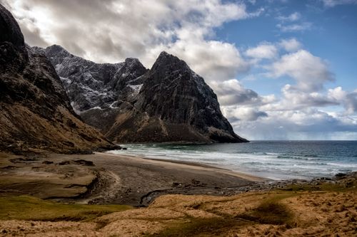 Free Spectacular scenery of sandy beach of waving  ocean surrounded by rocky mountains with snowy slopes against cloudy sky in Norway Stock Photo