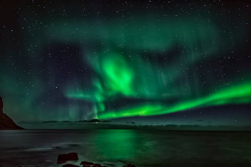 Starry night sky with green polar lights over waving ocean in mountainous terrain in winter