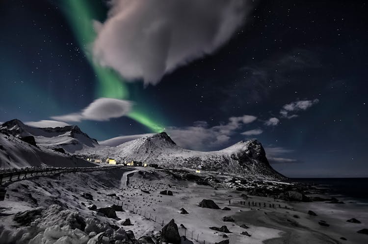 Aurora Borealis In Starry Night Above Snowy Mountains At Seaside