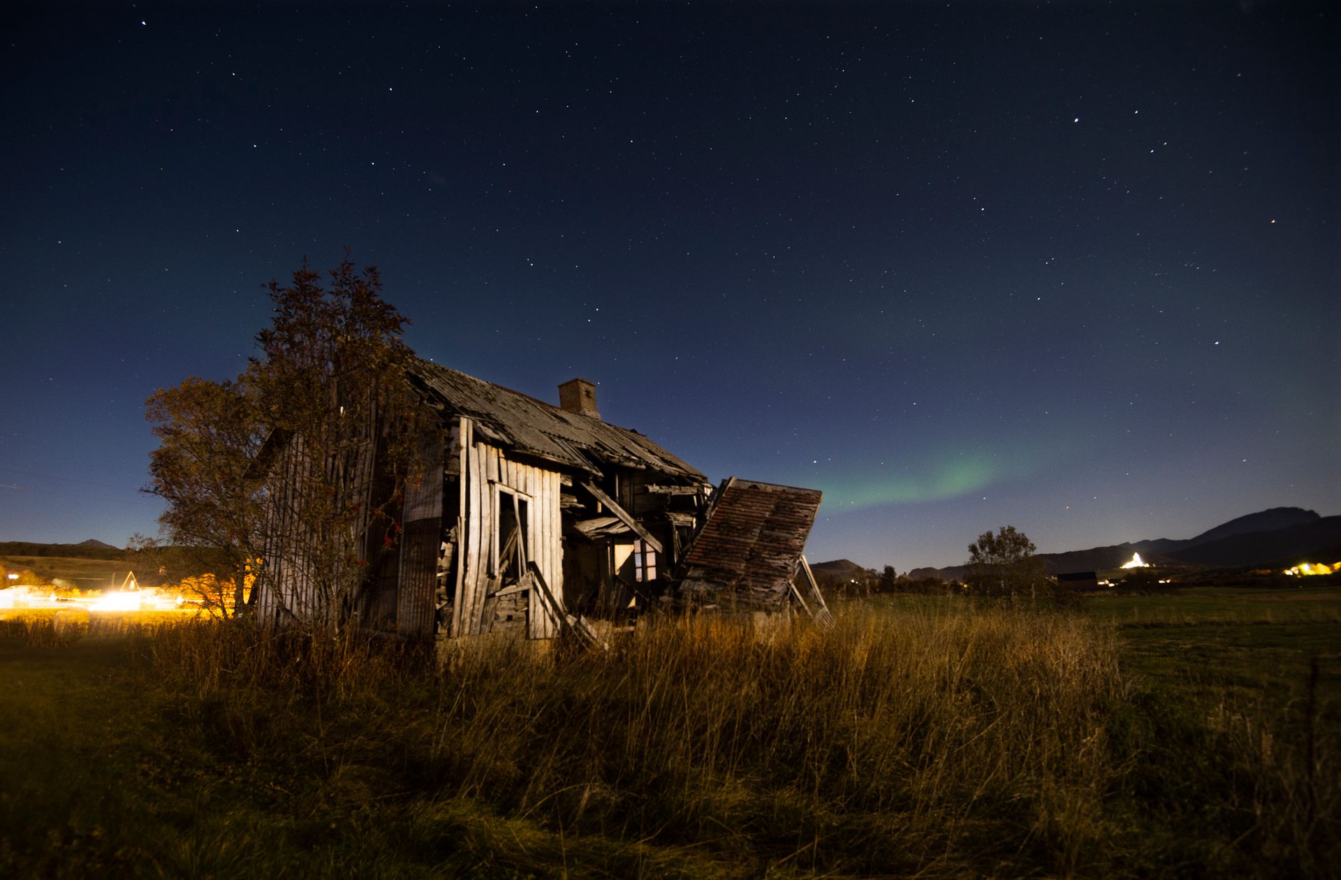 Old ruined hut located on grassy field in countryside against night starry sky with northern light in Norway