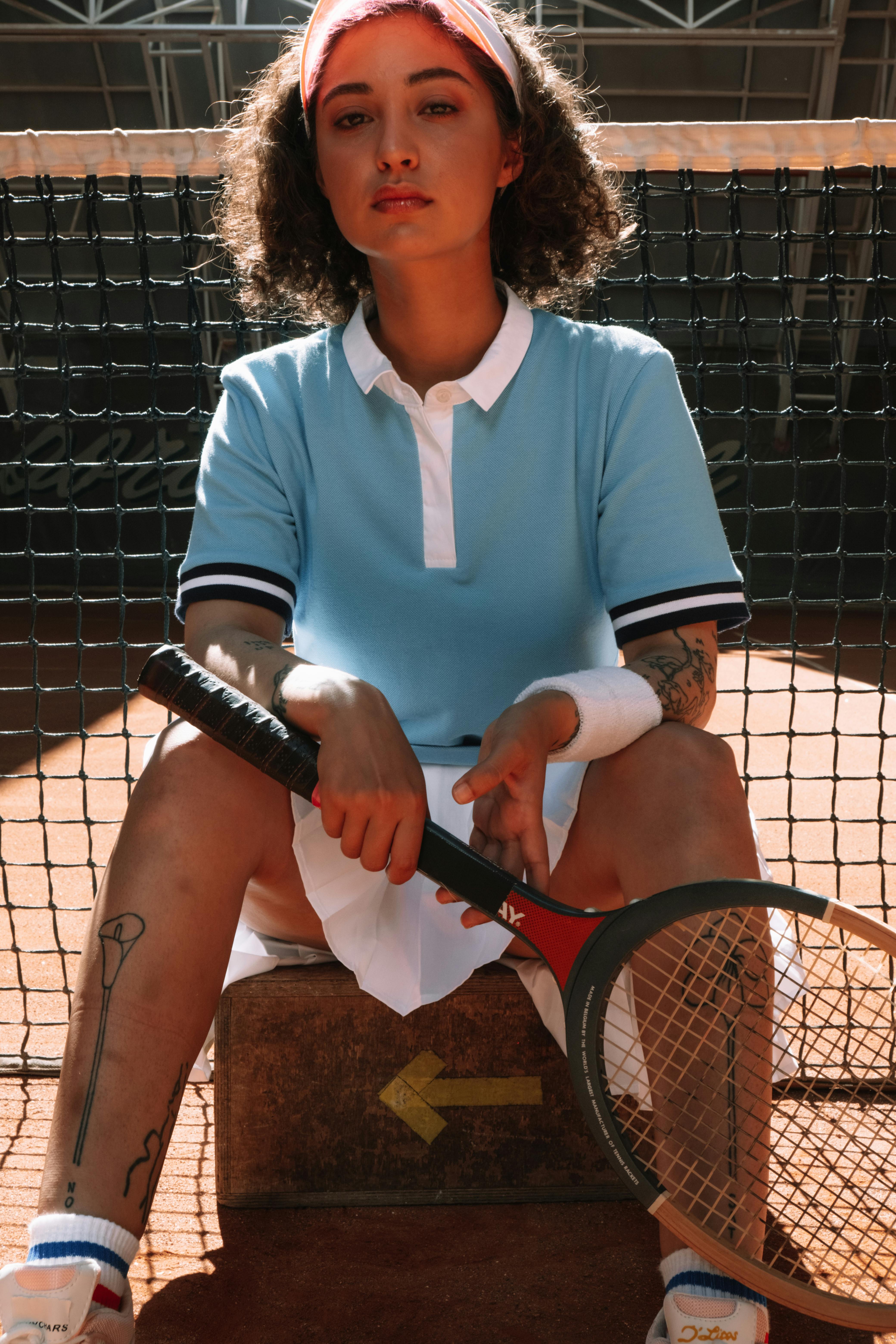 Stylish female tennis player with racket, seated on clay court, exuding confidence and style.
