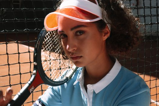 Close-up of a young female tennis player with racket on clay court.