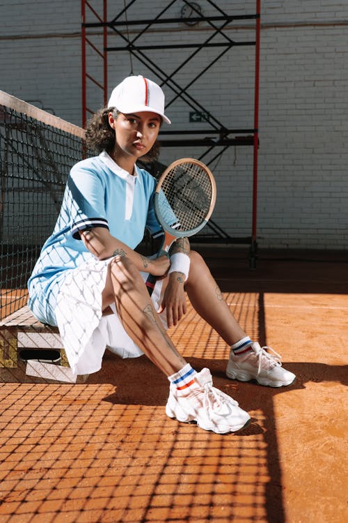 A Woman Sitting on the Clay Court while Holding a Tennis Racket