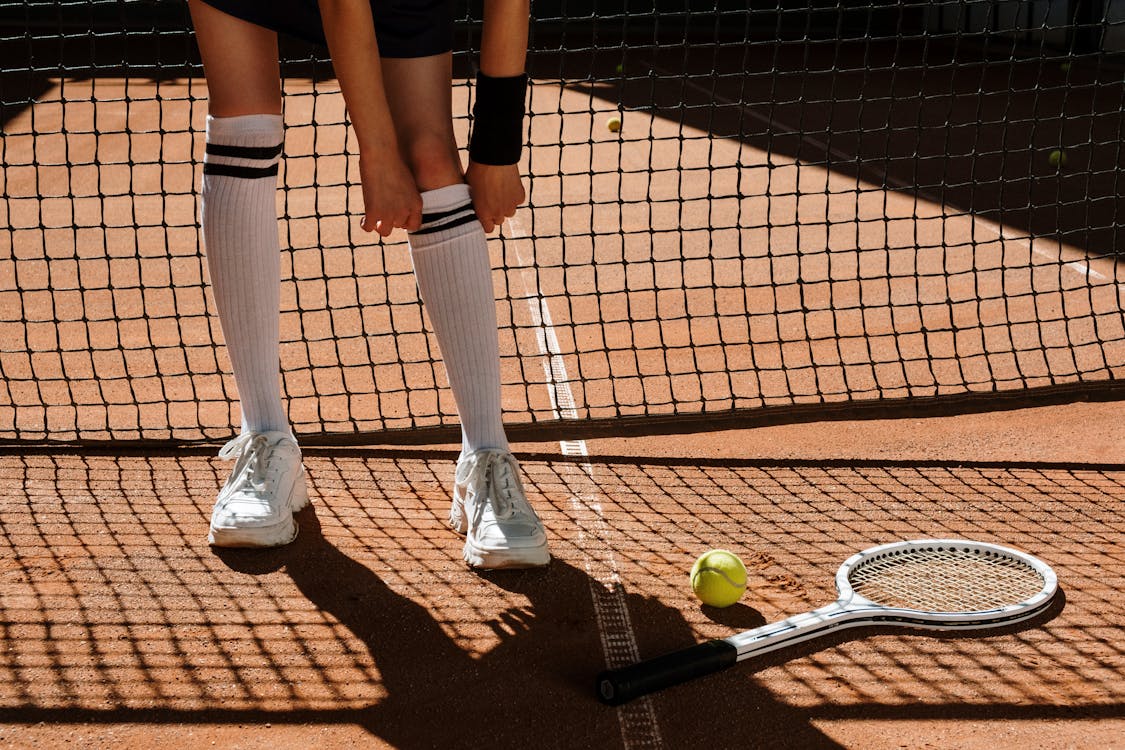 Person in Black Shorts and Black Socks Standing on Brown and White Tennis Court