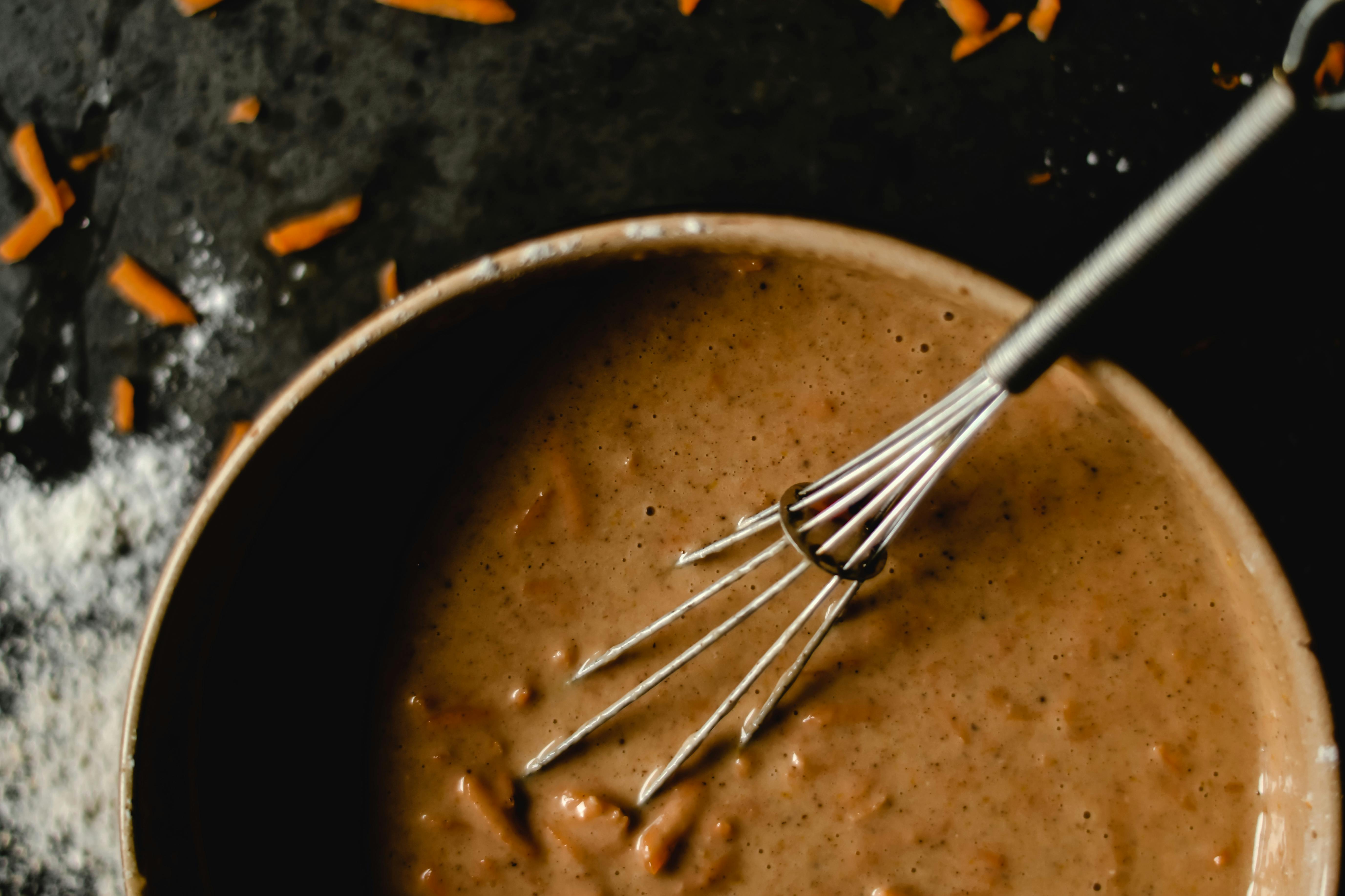 A bowl of carrot cake batter with whisk, showcasing baking ingredients and preparation.