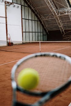 Close-up view of a tennis racket and ball on an indoor clay court, showcasing the sport's dynamics.