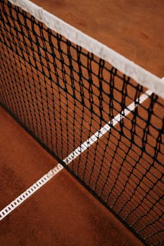 Detailed close-up of a tennis net on a clay court with white lines.