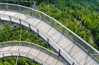 航拍捕捉到了郁郁葱葱的绿色森林中一座现代弯曲木桥的风景，展现了优美的自然景观