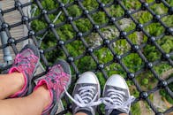 两个穿着运动鞋的人站在索网桥上，桥下是郁郁葱葱的森林