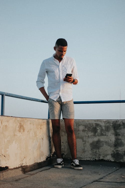 Free Confident young African American male relaxing on terrace and using smartphone Stock Photo