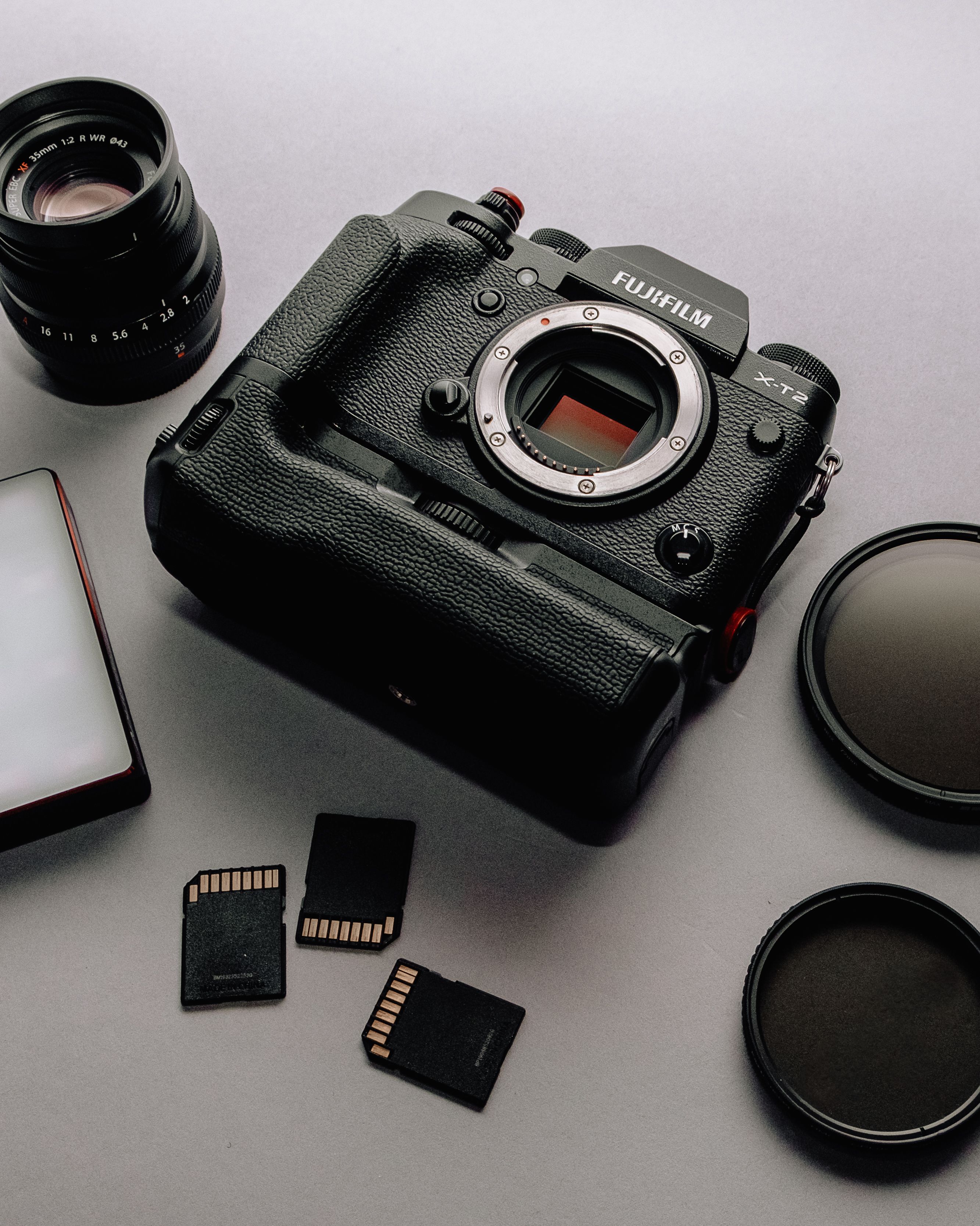 Flat lay photography of camera gear including lens and memory cards on a neutral surface.